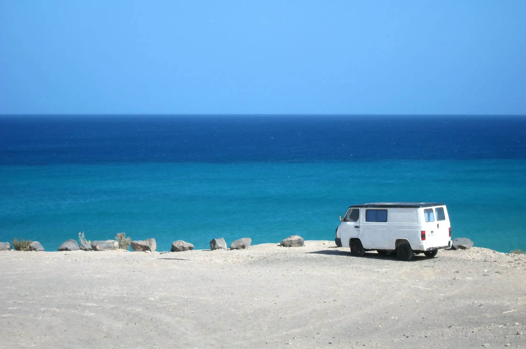 White campervan parked on a sandy beach above turquoise water