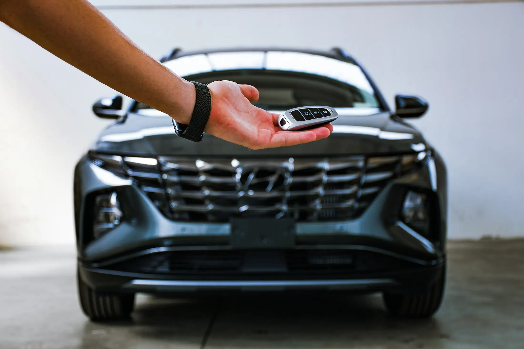A hand presenting a smart key in front of the grille of a brand-new dark grey SUV