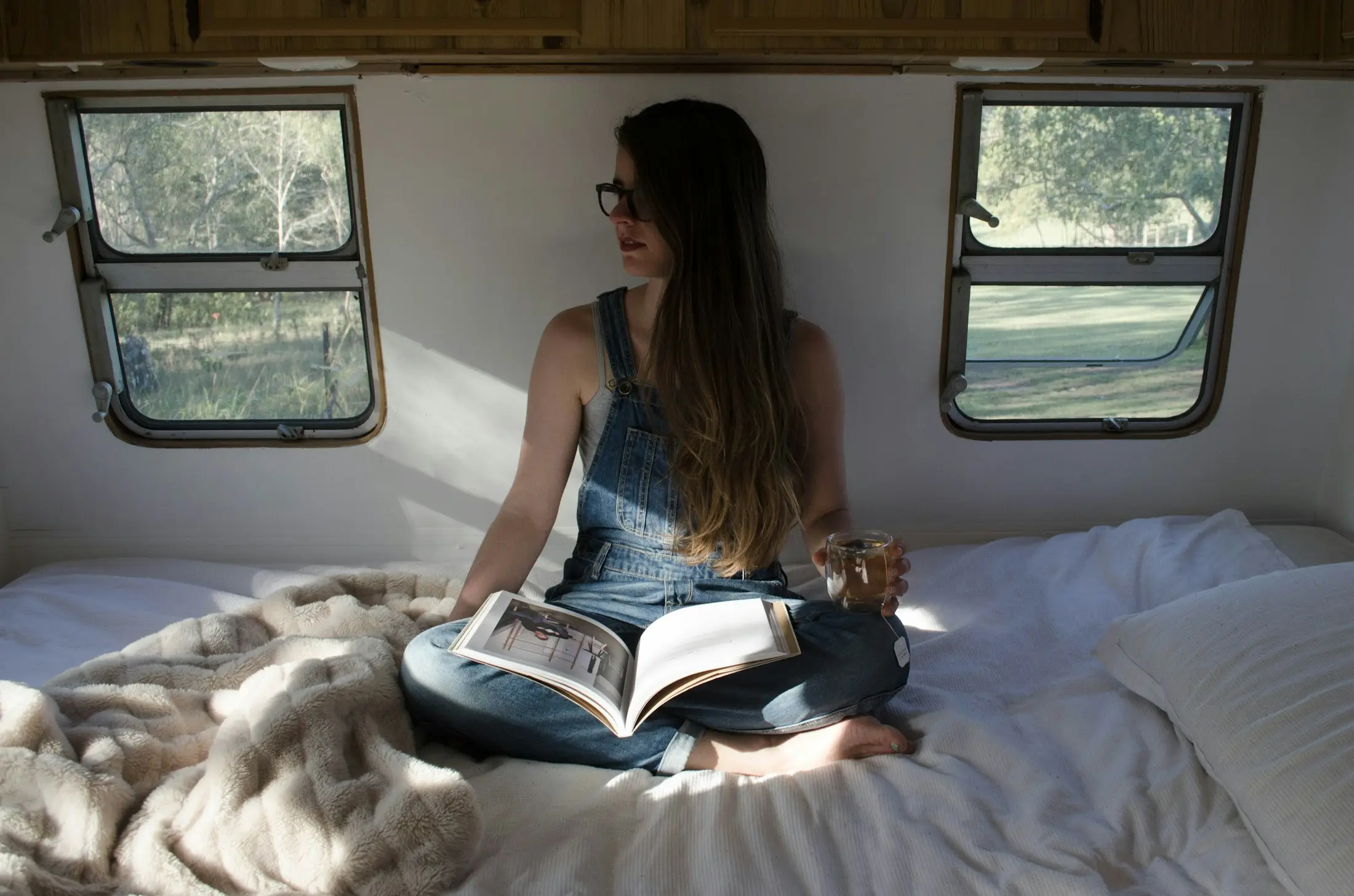 Woman reading on a cosy bed inside a caravan