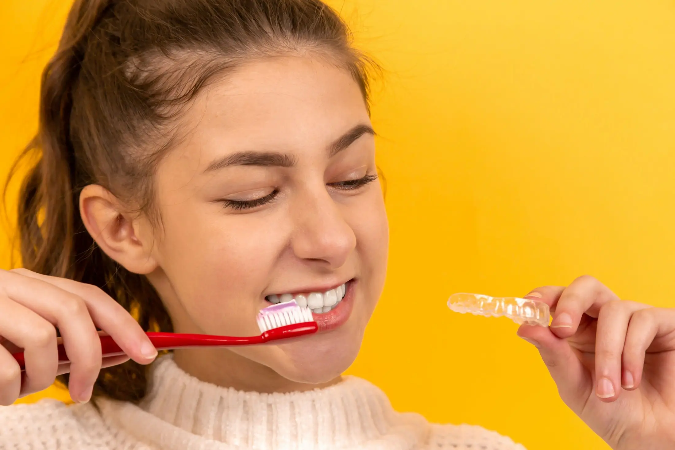 Smiling young woman holding a toothbrush and clear aligner