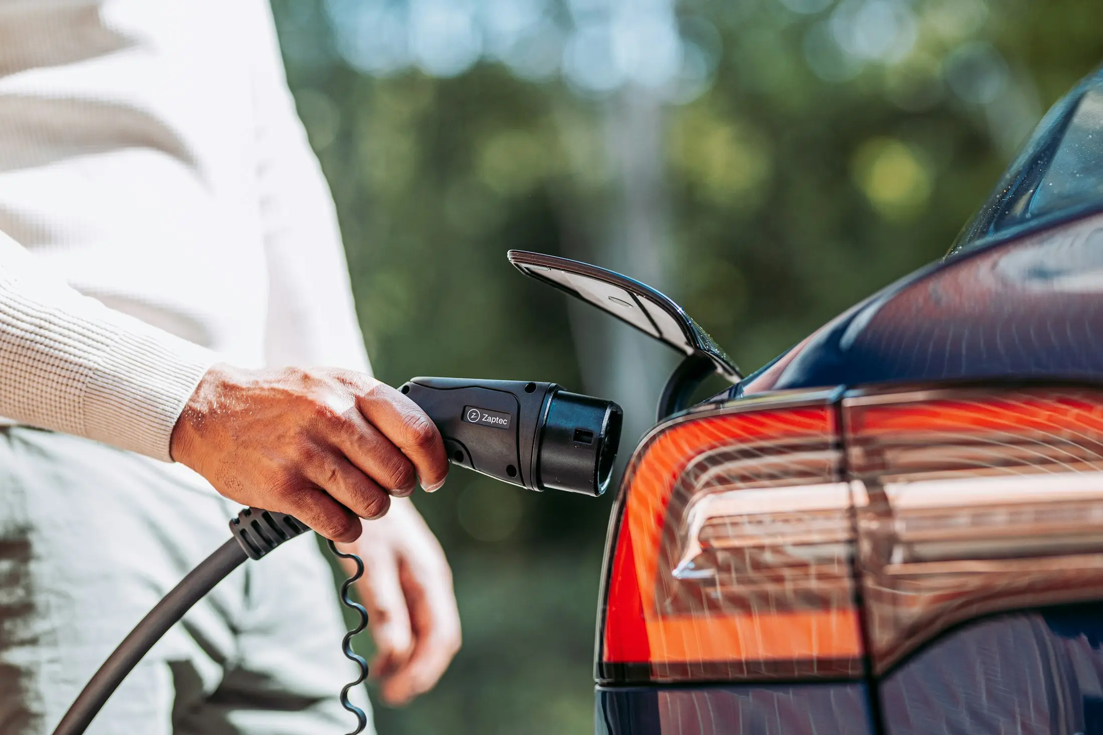 Hand plugging a charging cable into an electric car