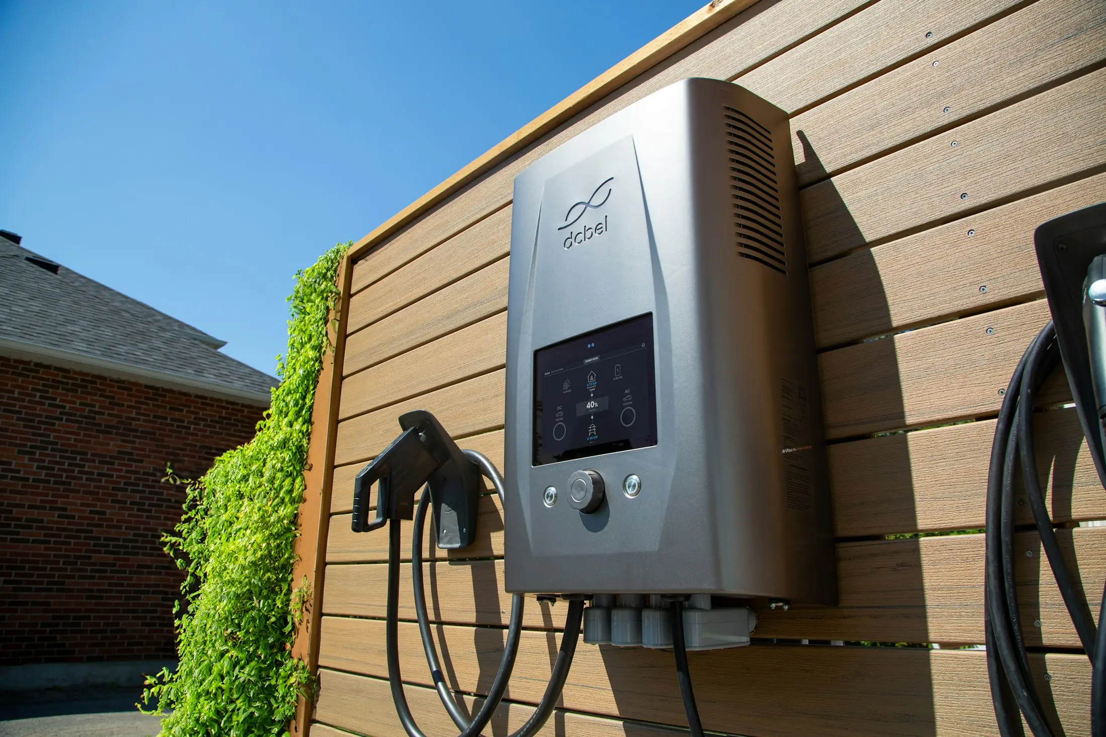 Wall-mounted home EV charger with coiled cables on a timber fence in the sun