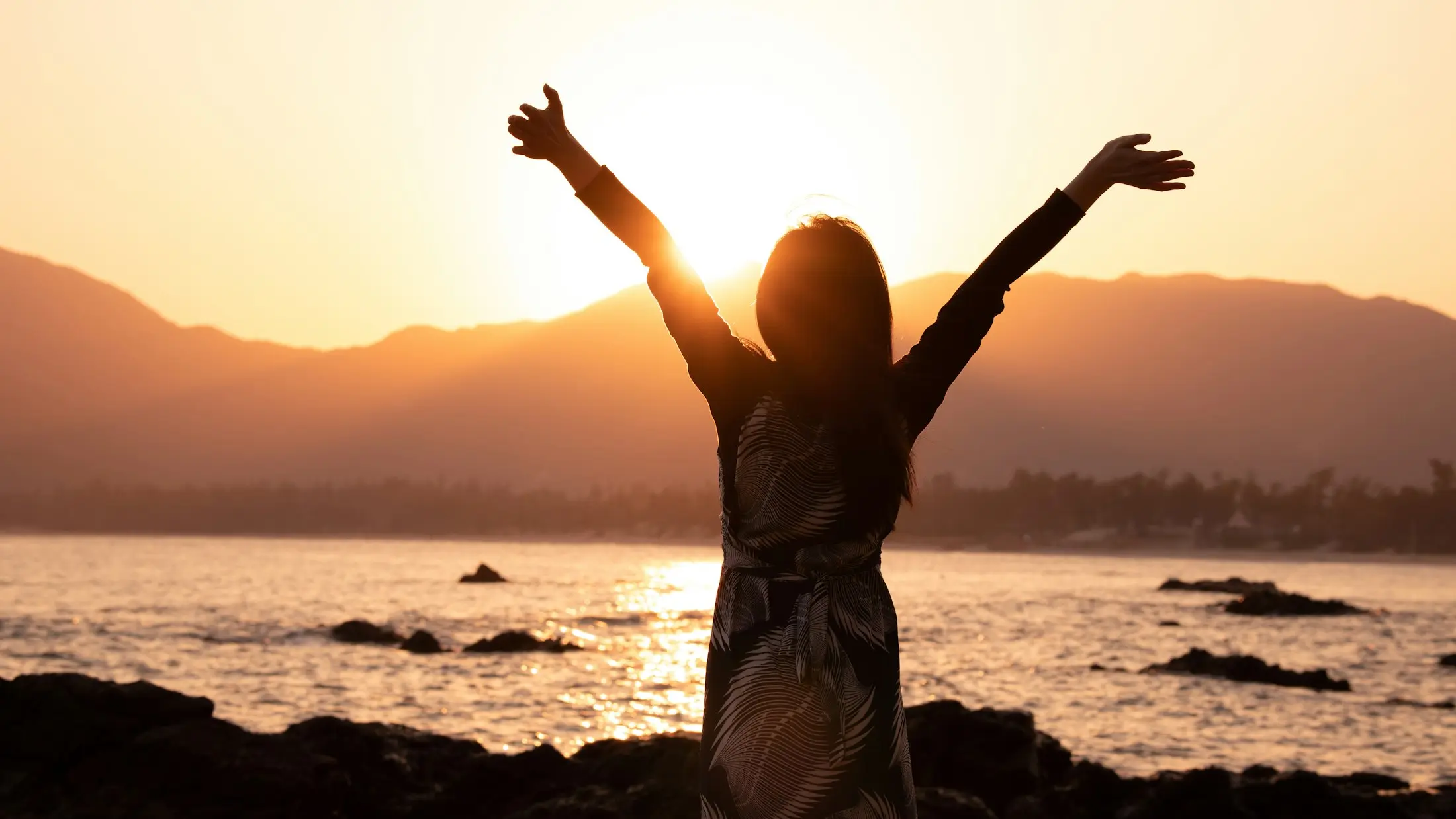 Woman with arms raised watching the sun set over the ocean