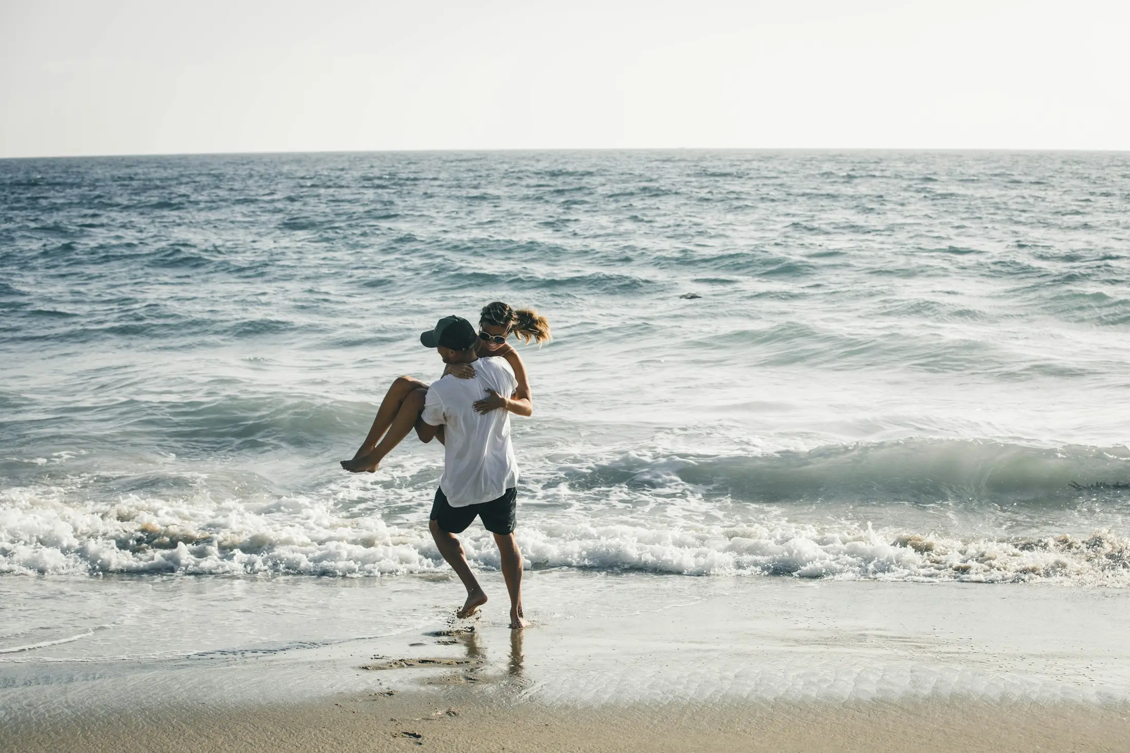 Couple laughing as he carries her through the shallow surf