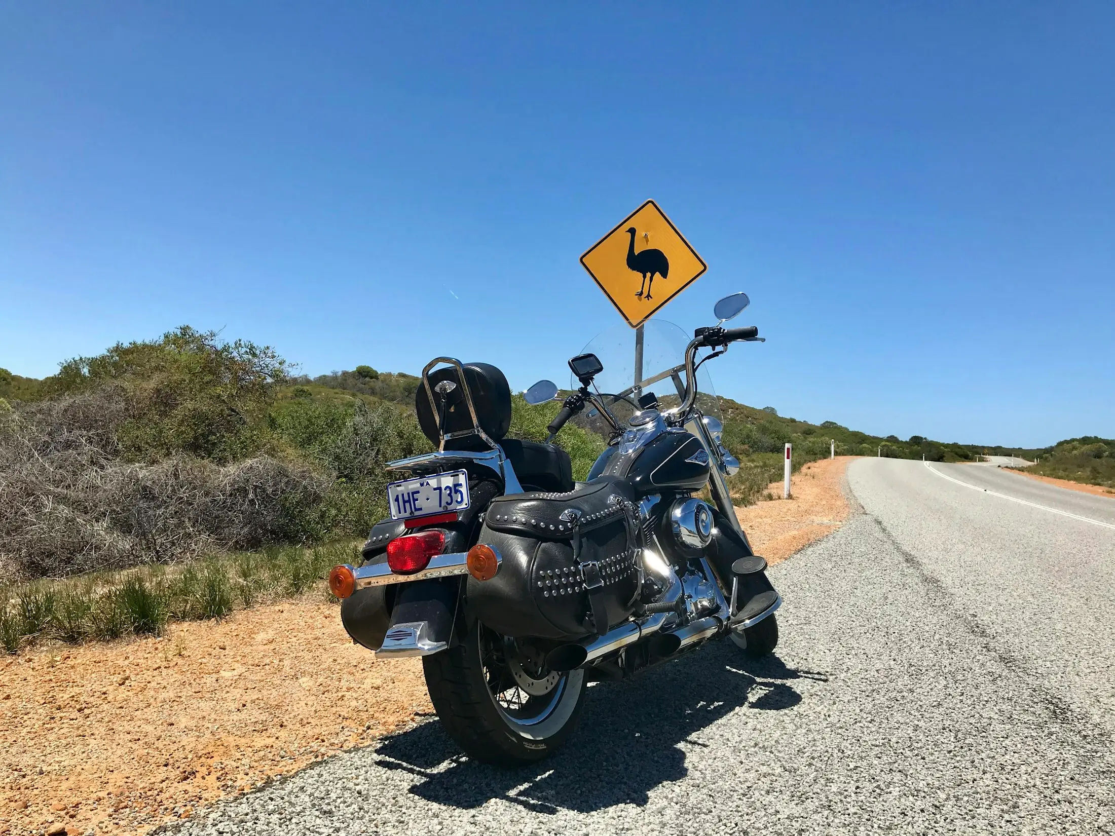 Cruiser motorbike parked on the shoulder of a sunny coastal road beside a yellow emu warning sign