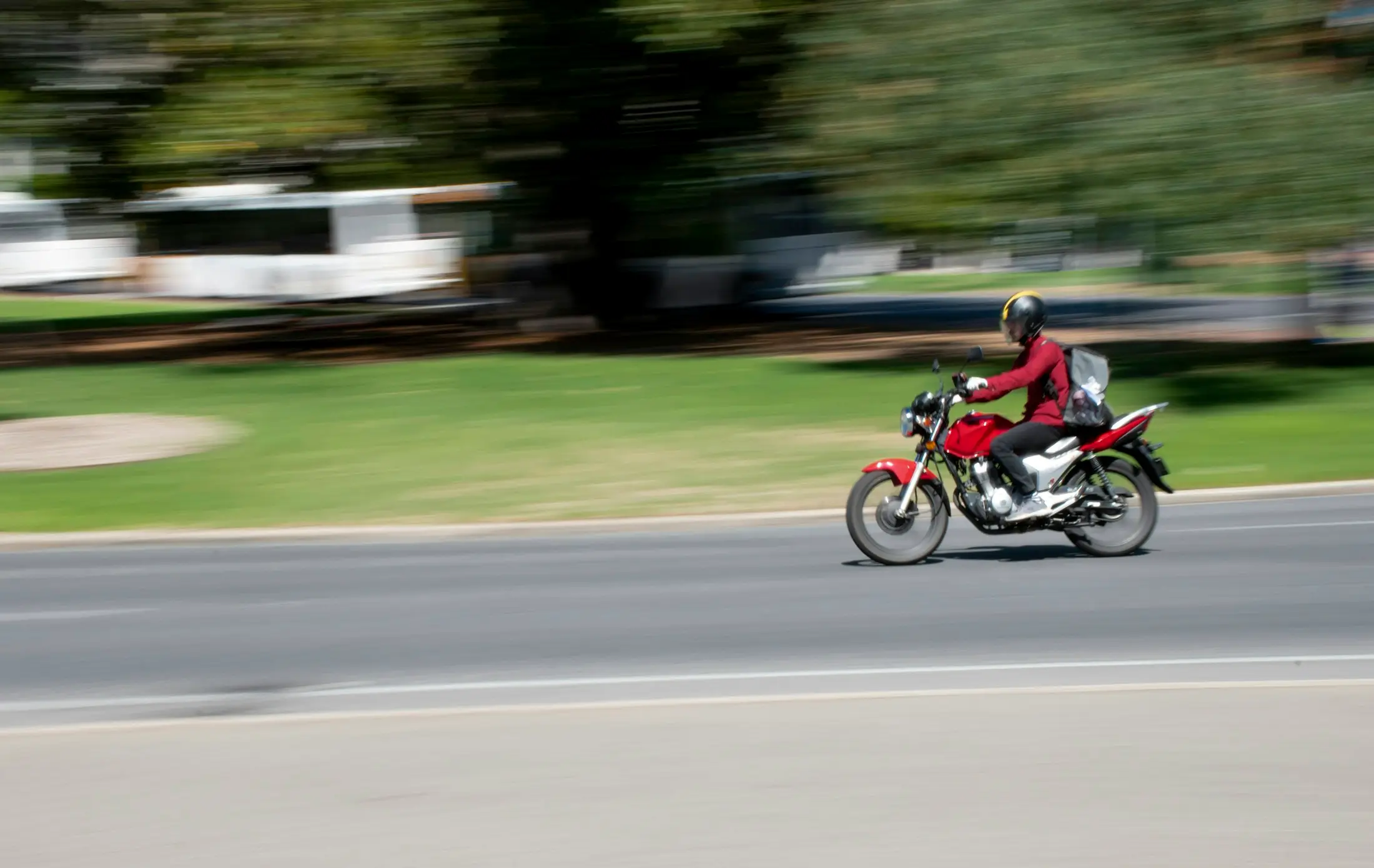 Rider on a red motorbike speeding along a tree-lined road
