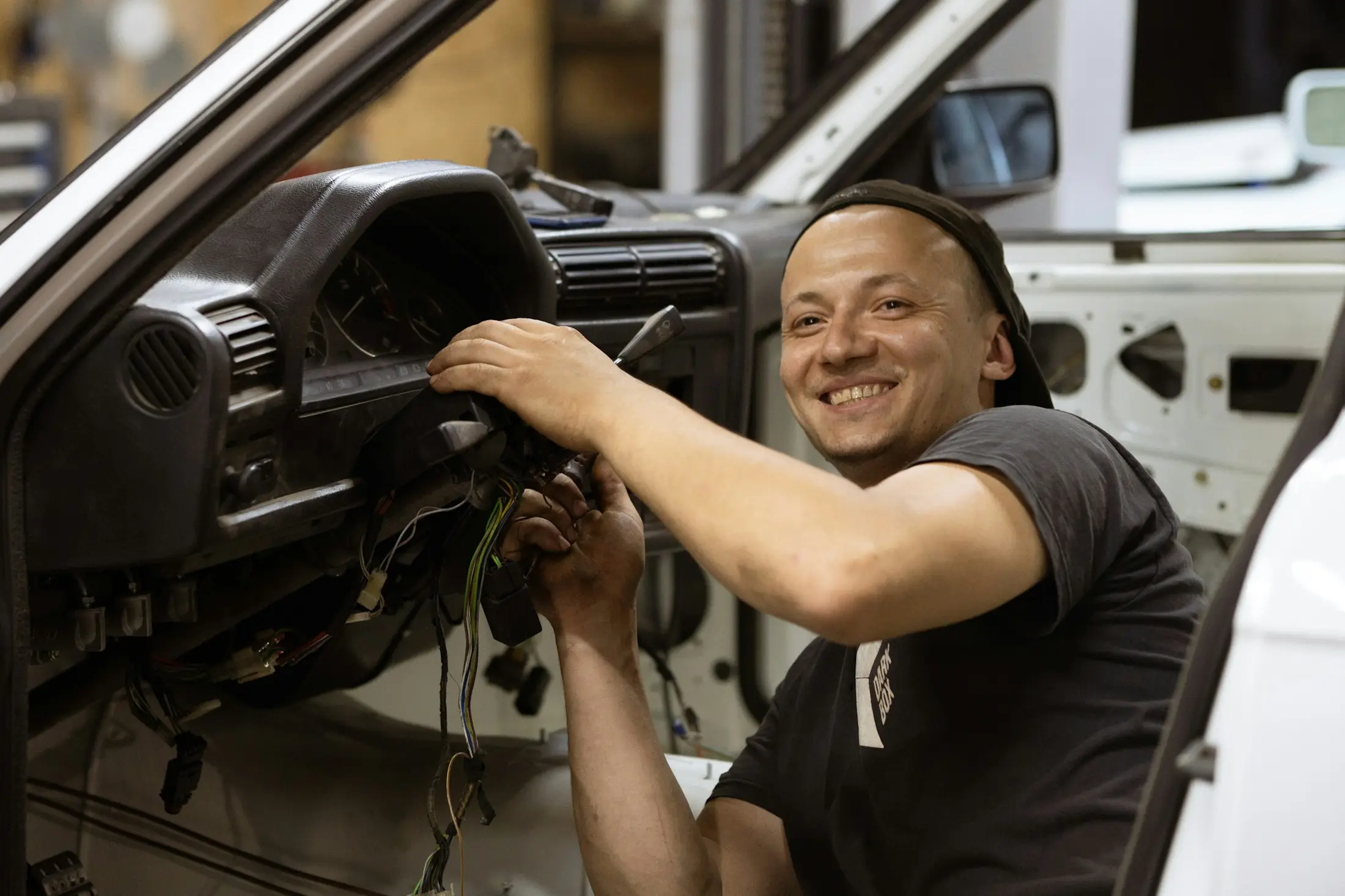 Grinning mechanic repairing the wiring under a car’s dashboard
