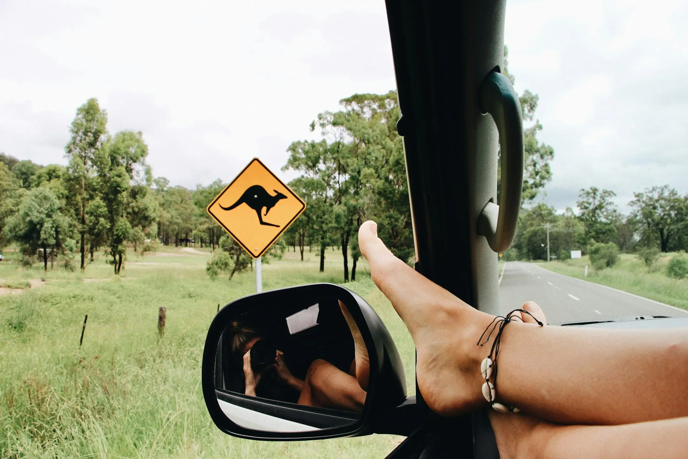 Feet up out of a car window on an Australian country road, passing a yellow kangaroo road sign