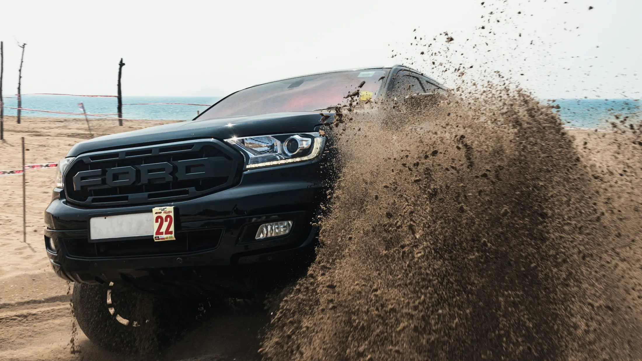 Black ute kicking up sand on a beach drive