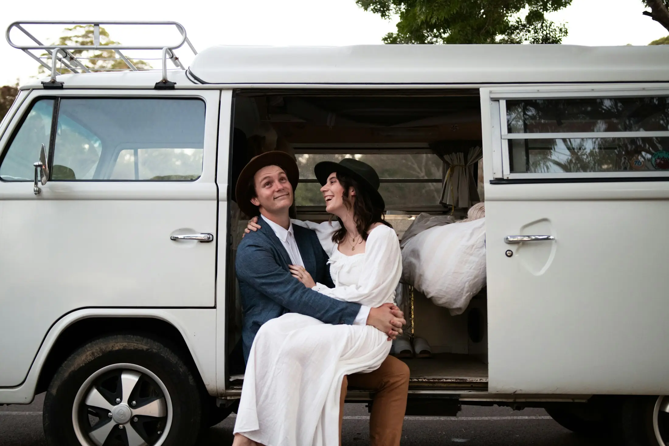 Newlywed couple sitting together in the open doorway of a vintage white Kombi van